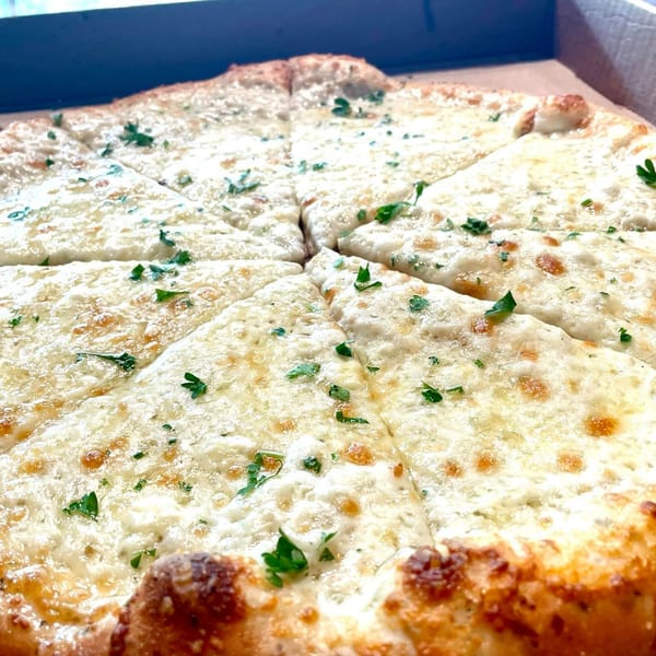 A white pizza from Lucy Blue Pizza, topped with melted cheese and fresh parsley, sliced in a box.