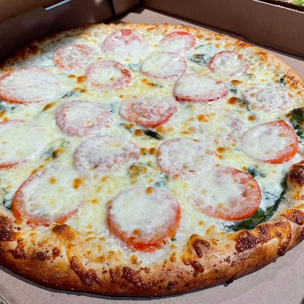 A whole Lucy Blue Pizza with melted cheese, tomato slices, and spinach in a delivery box.